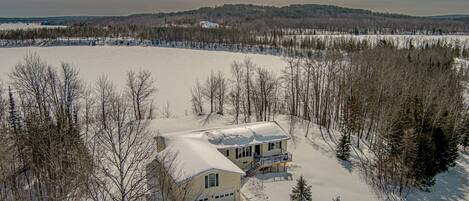 A snow-covered landscape with a house surrounded by trees.