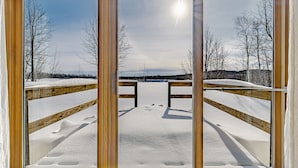 A wooden deck leading to a snowy landscape with bare trees and a clear sky.
