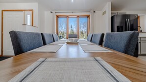 A modern dining room with a long wooden table, grey upholstered chairs, and a central bowl.