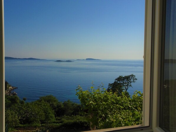 A view of a calm sea with distant islands, framed by lush greenery.