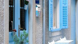 Eine Gebäudefassade mit einer blauen Tür, einem Fenster mit blauen Rollläden und einem Schild, das eine Studio-Wohnung anzeigt.