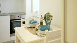 Une table à manger dressée avec des bols bleus, des verres à vin et une bouteille de vin, dans une cuisine moderne aux armoires blanches et dotée d’un four encastré.