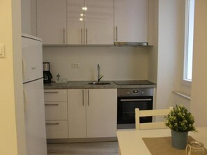 A compact kitchen with a refrigerator, stove, sink, and a small dining area with a table and chair.