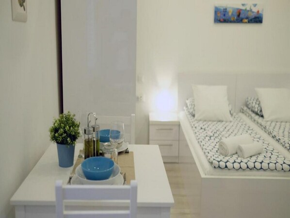 A bedroom with a bed, bedside table, and a small table with a plant and glasses.