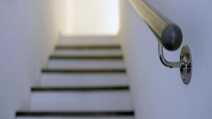 Une main courante en métal, dotée d’une poignée ronde et fixée au mur, qui mène à un escalier.