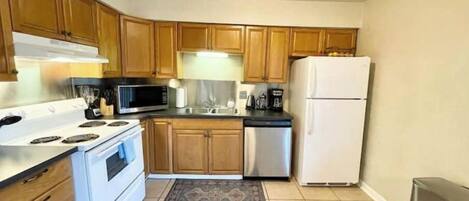 A compact kitchen with wooden cabinets, a white stove, a microwave, a refrigerator, and a coffee maker.