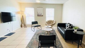 A living room with a black sofa, a black chair, a small round table, a floor lamp, and a television on the wall. - Relax South Central *5 mi from downtown* VB (Austin)