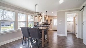 A spacious kitchen with large windows, a dining area with a table and chairs, and a hallway leading to a door. - Perfect Lake House Getaway! (Waterford)