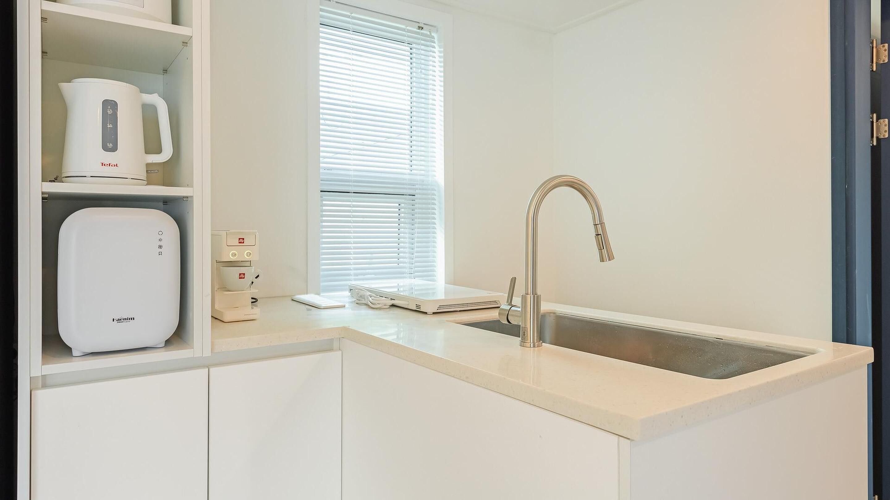 A modern kitchen with a built-in coffee maker, a kettle, a scale, and a sink.
