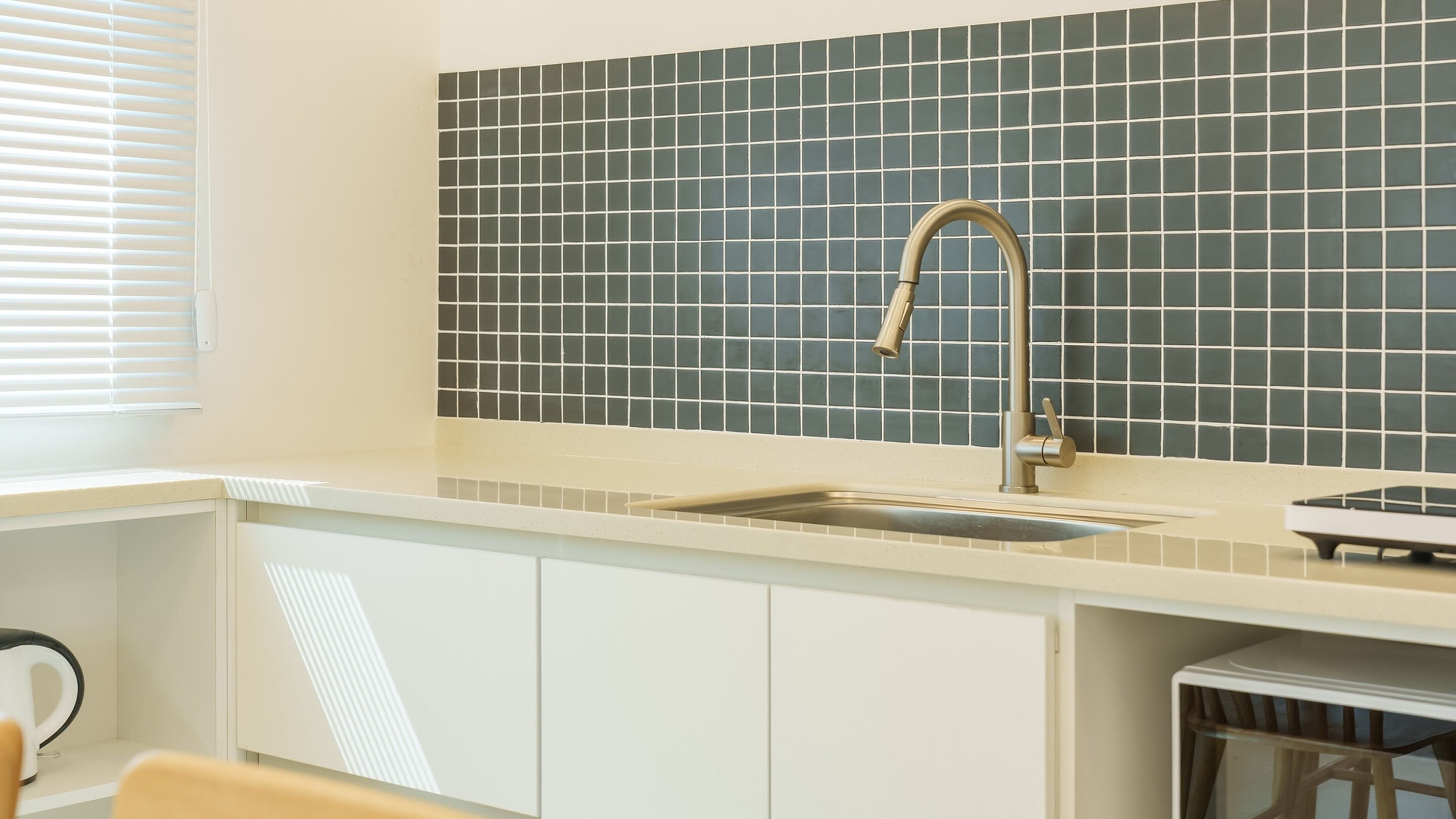 A kitchen with a sink, a window with blinds, and a tiled backsplash.
