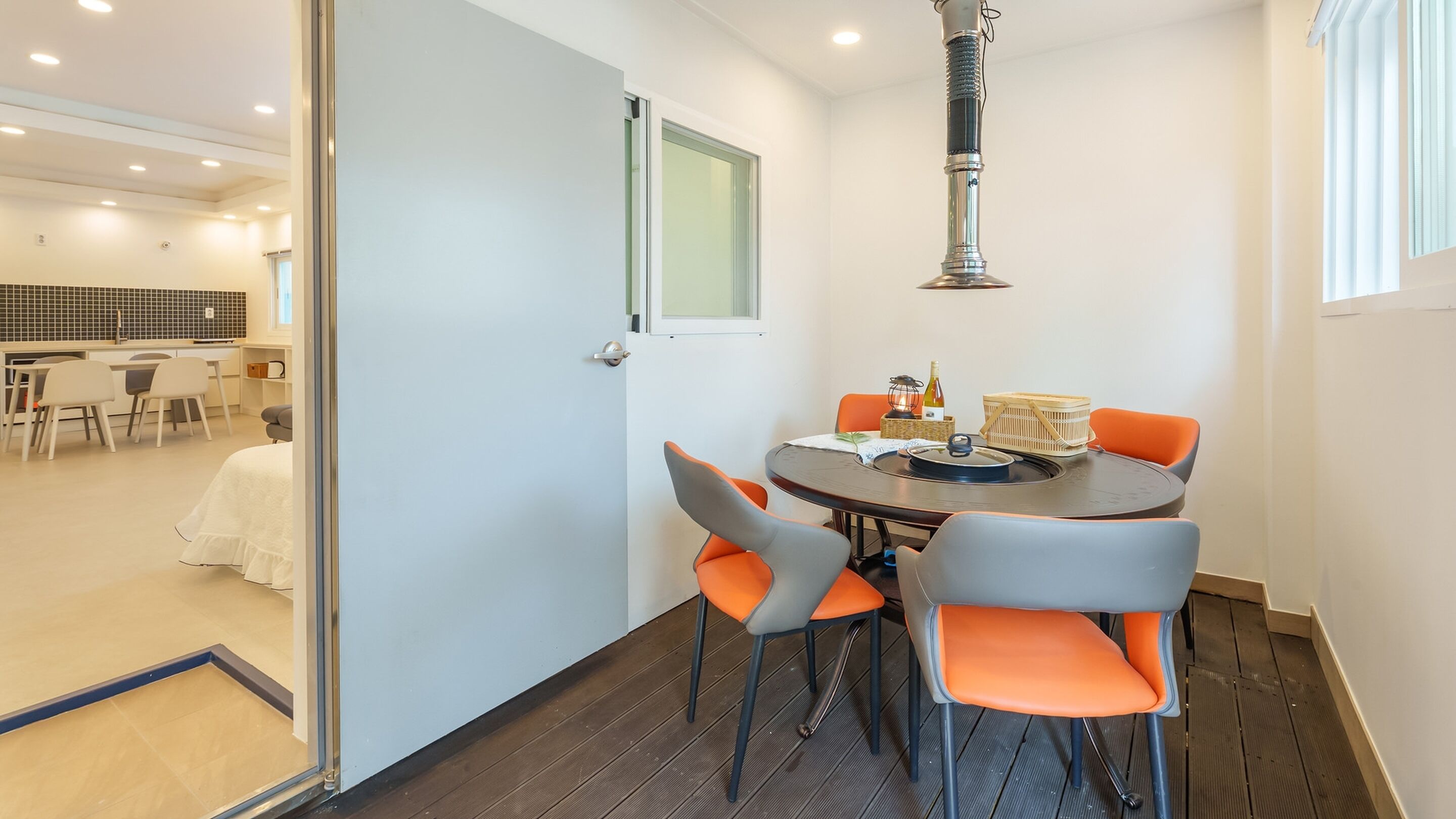 A modern dining area with a round table, orange chairs, and a hanging light fixture.