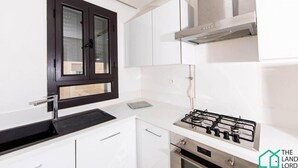 Une cuisine avec des armoires blanches, une fenêtre à cadre noir, une hotte de cuisine en acier inoxydable et une cuisinière à gaz.