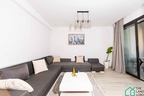 Una sala de estar moderna con un sofá seccional, una mesa de centro, un cuadro y un ventanal con cortinas.