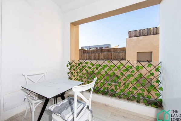 Un balcón con mesa y sillas, una valla de madera y vistas a edificios al fondo.