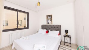 Une chambre à coucher avec un grand lit, une fenêtre, une table de chevet et un luminaire fixé au mur.