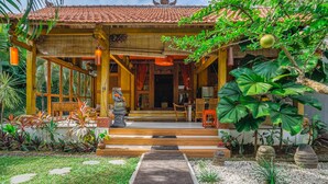 A traditional wooden house with a tiled roof, a wooden porch, and a stone pathway leading to the entrance. - Villa Pagoda (Legian)