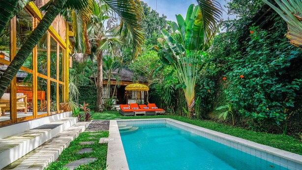 A swimming pool surrounded by lush greenery and a wooden structure with large windows. - Villa Pagoda (Legian)