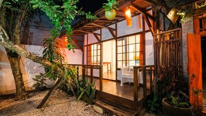 A rustic wooden cabin with a porch, surrounded by plants and a tree. - Villa Pagoda (Legian)
