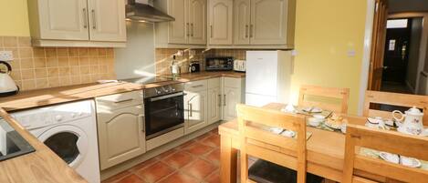 A compact kitchen with a washing machine, oven, microwave, and a dining area with a table and chairs.