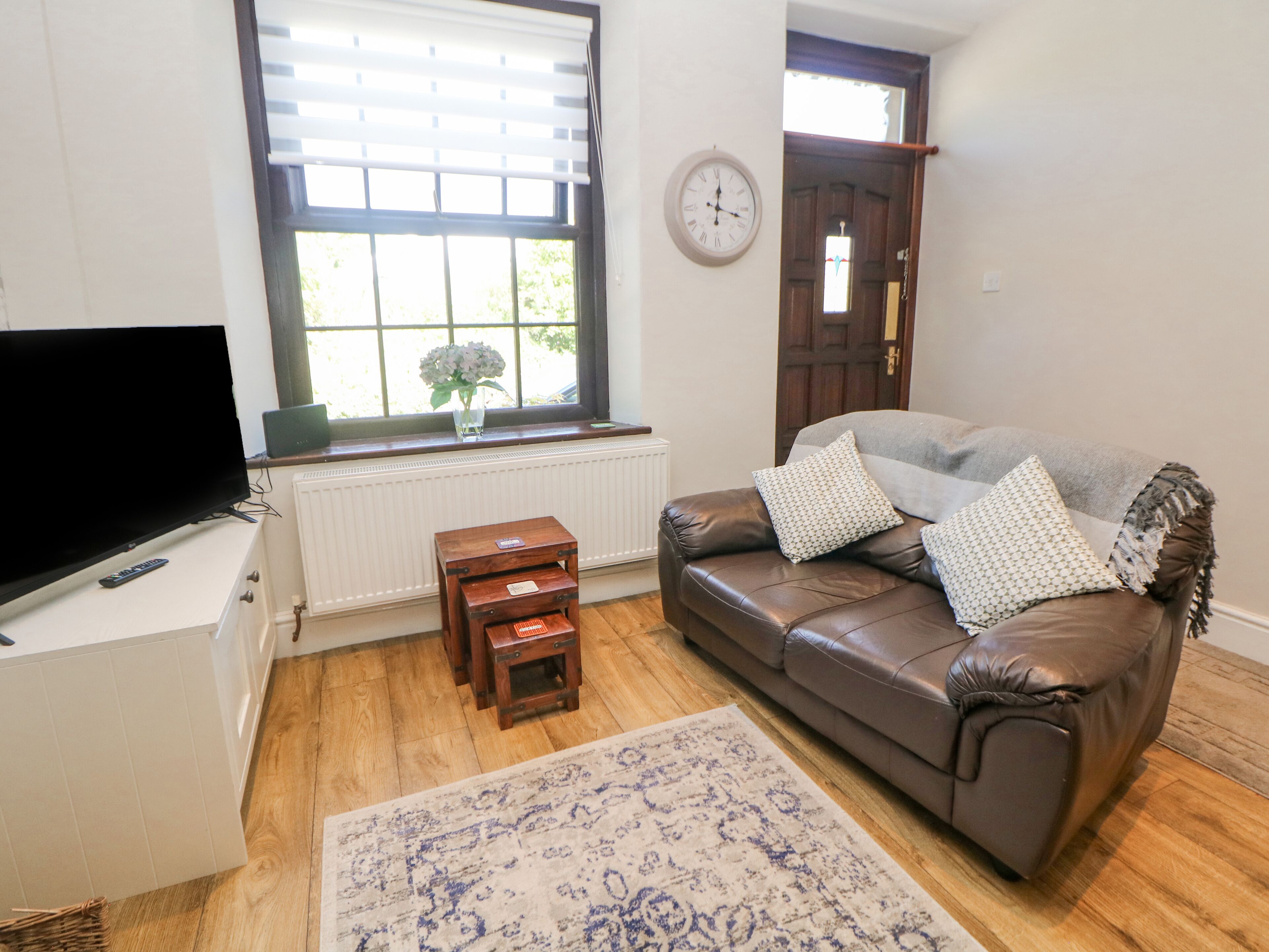 A living room with a brown leather sofa, a small wooden table, a TV, and a window with blinds.