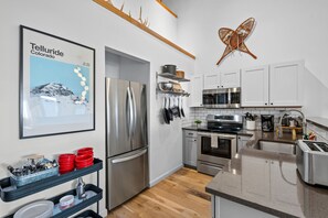 A modern kitchen with stainless steel appliances, a hanging pot rack, and a framed picture of Telluride, Colorado. - Chalet Chic Condo, Short Walk To Lift 7, Covered Parking 2 Bedroom Condo by RedAwning (Telluride)