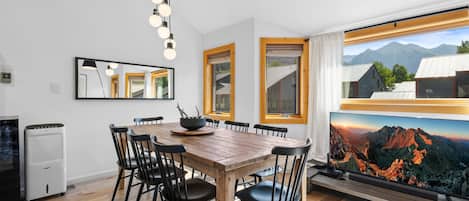 A dining area with a wooden table and chairs, a large window with a mountain view, and a modern kitchen with a built-in oven.