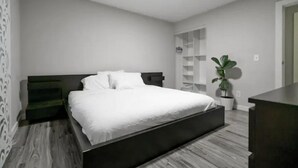 Ein modernes Schlafzimmer mit einem großen Bett, einem Nachttisch, einem Kleiderschrank und einer Topfpflanze.