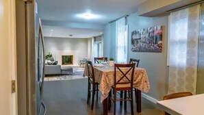 Ein Essbereich mit einem Tisch für vier Personen, einer Couch im Hintergrund und einem Bild an der Wand.