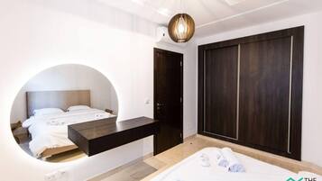 A modern bedroom with a bed, a circular mirror, a dark wooden wardrobe, and a hanging light fixture.