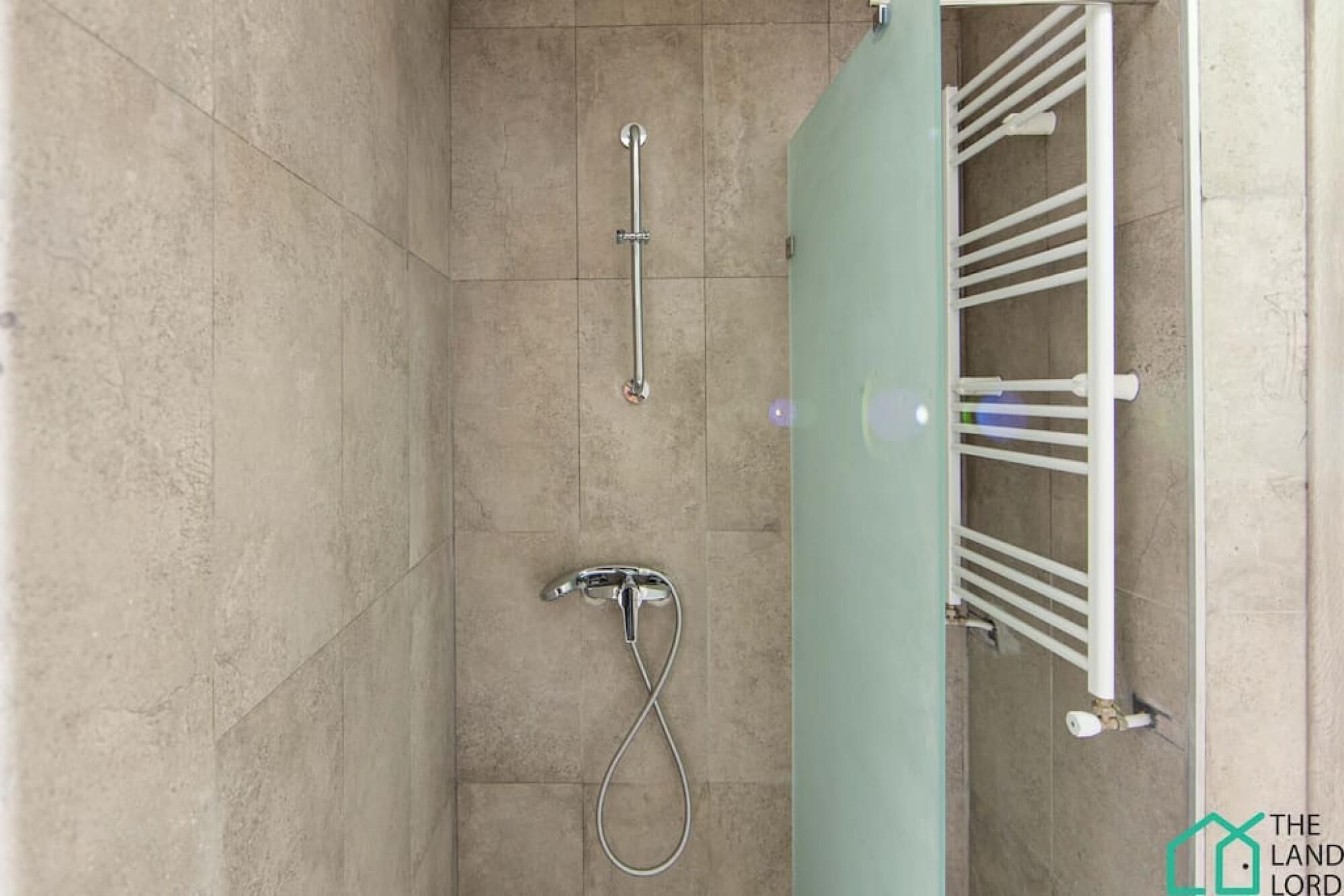Une salle de bain dotée d’une douche à parois de verre, d’un porte-serviettes blanc et d’un pommeau de douche à main.