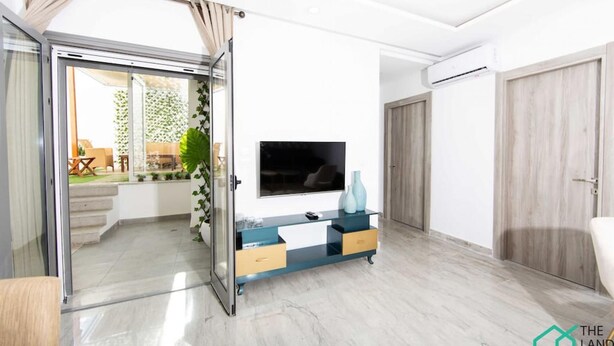 A modern living room with a sliding glass door leading to a patio, a flat-screen TV mounted on the wall, and a minimalist wooden door. - New 1bd With Swimming Pool 5mn to Lac Carthage (Tunis)