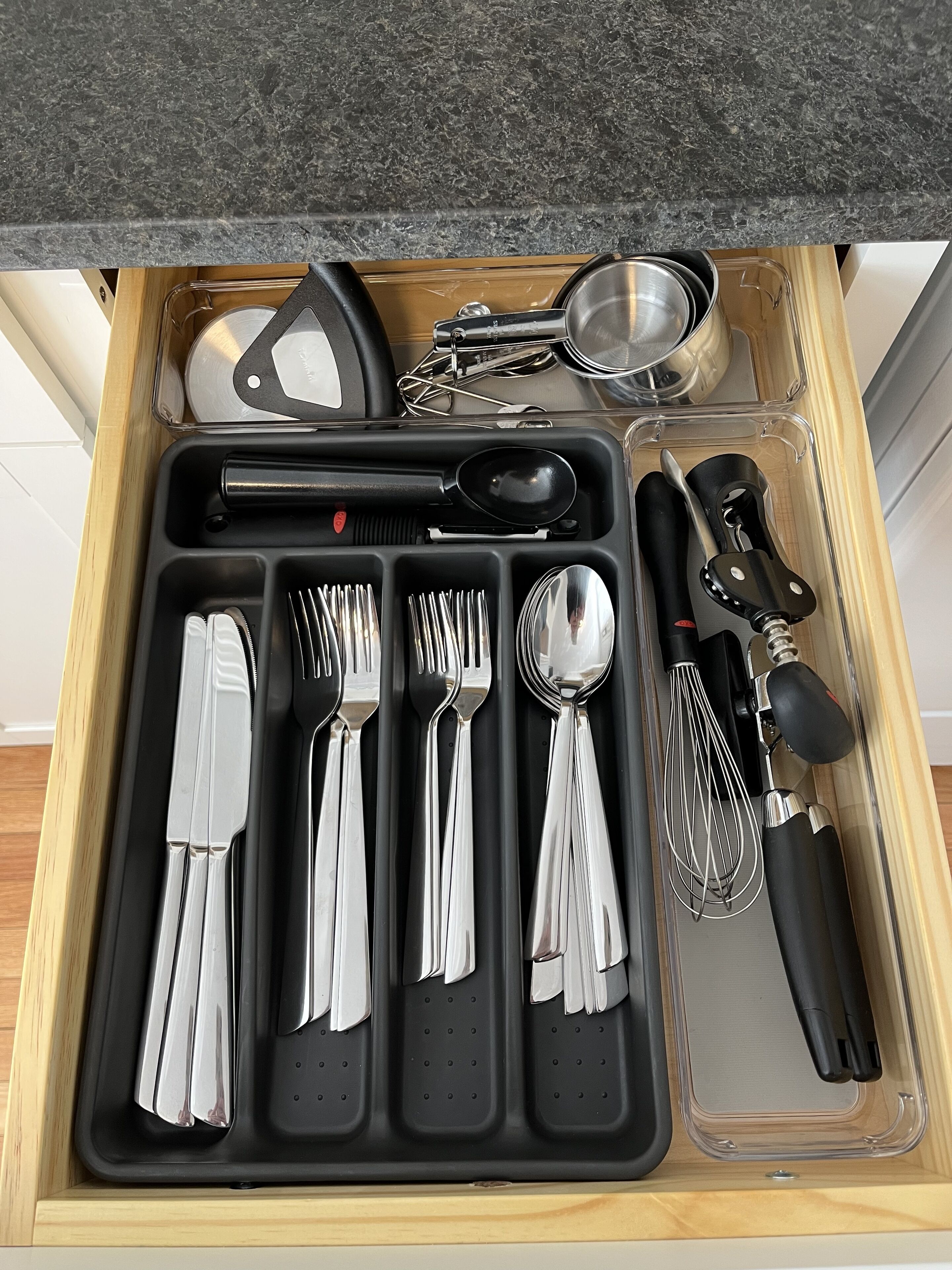 Un tiroir de cuisine contenant des ustensiles, notamment des fourchettes, des couteaux, des cuillères, un fouet et une râpe.