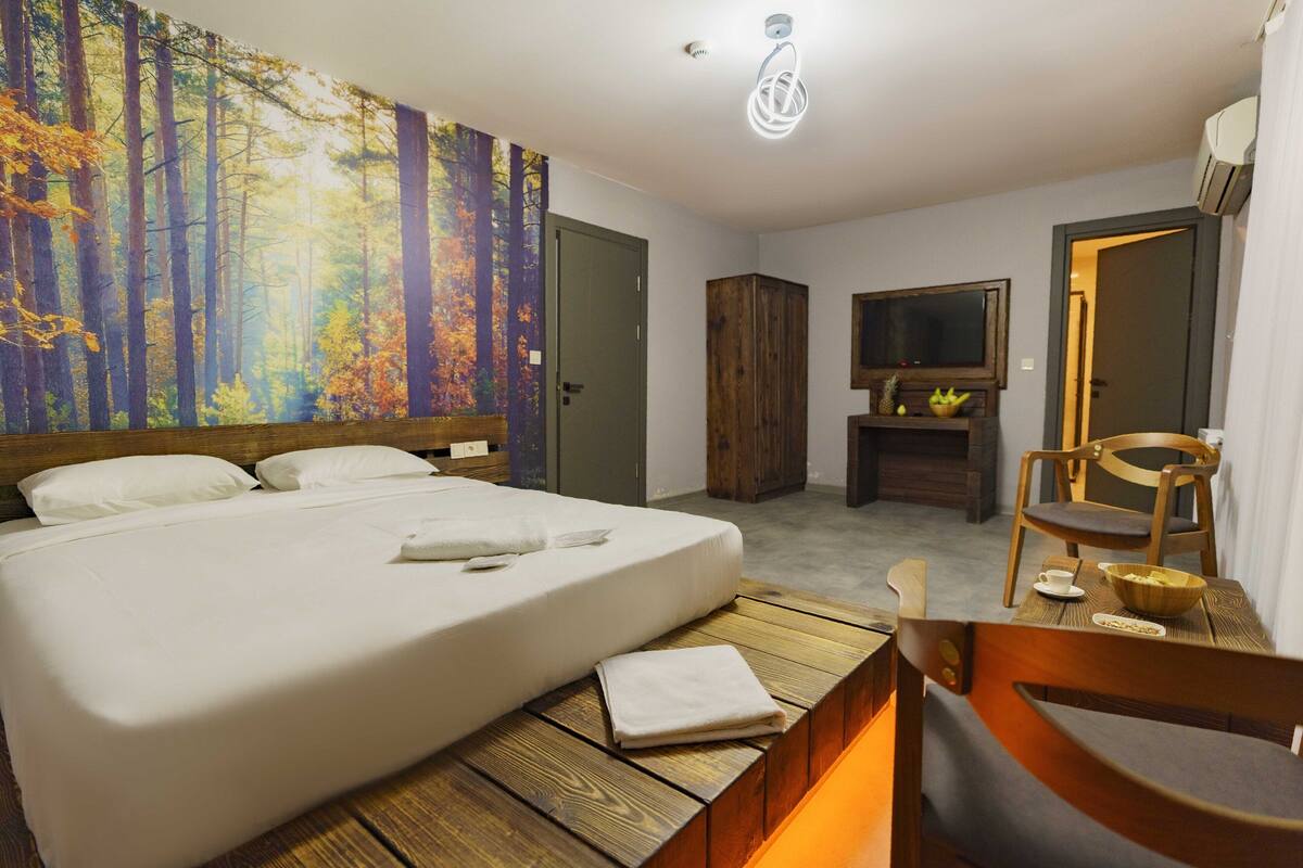 A hotel room with a bed, a television, a wooden cabinet, and a dining area with a chair and table.