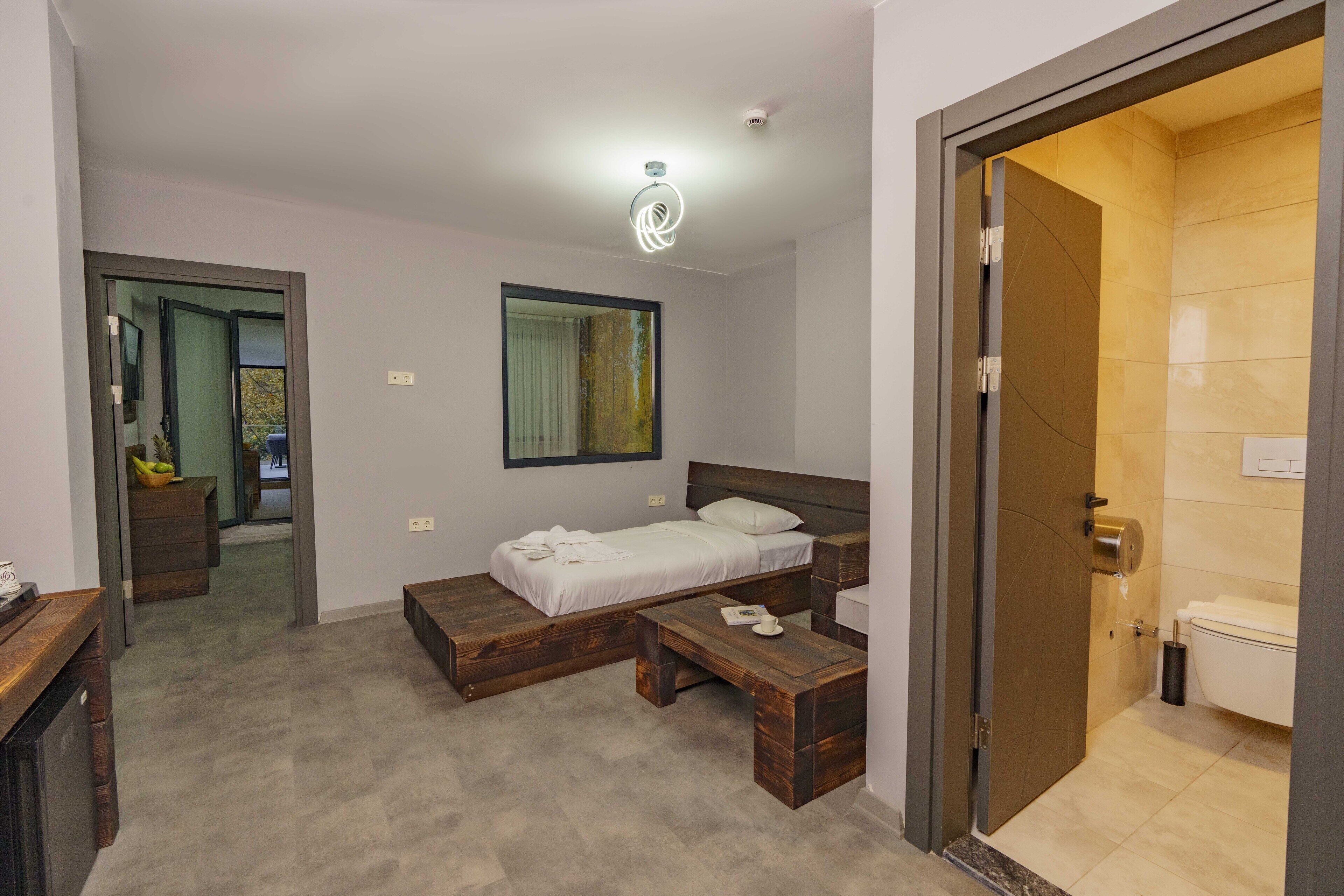 Ein Schlafzimmer mit Bett, Nachttisch und kleinem Schreibtisch. Es gibt ein Badezimmer mit Toilette und Dusche.
