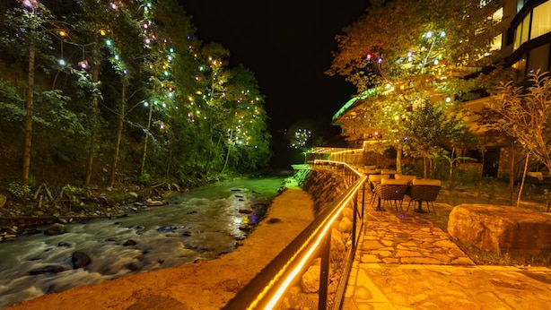 A nighttime riverside walkway with a stone path, wooden railings, and trees adorned with lights. - MacarTaşı Hotel  (Maçka)