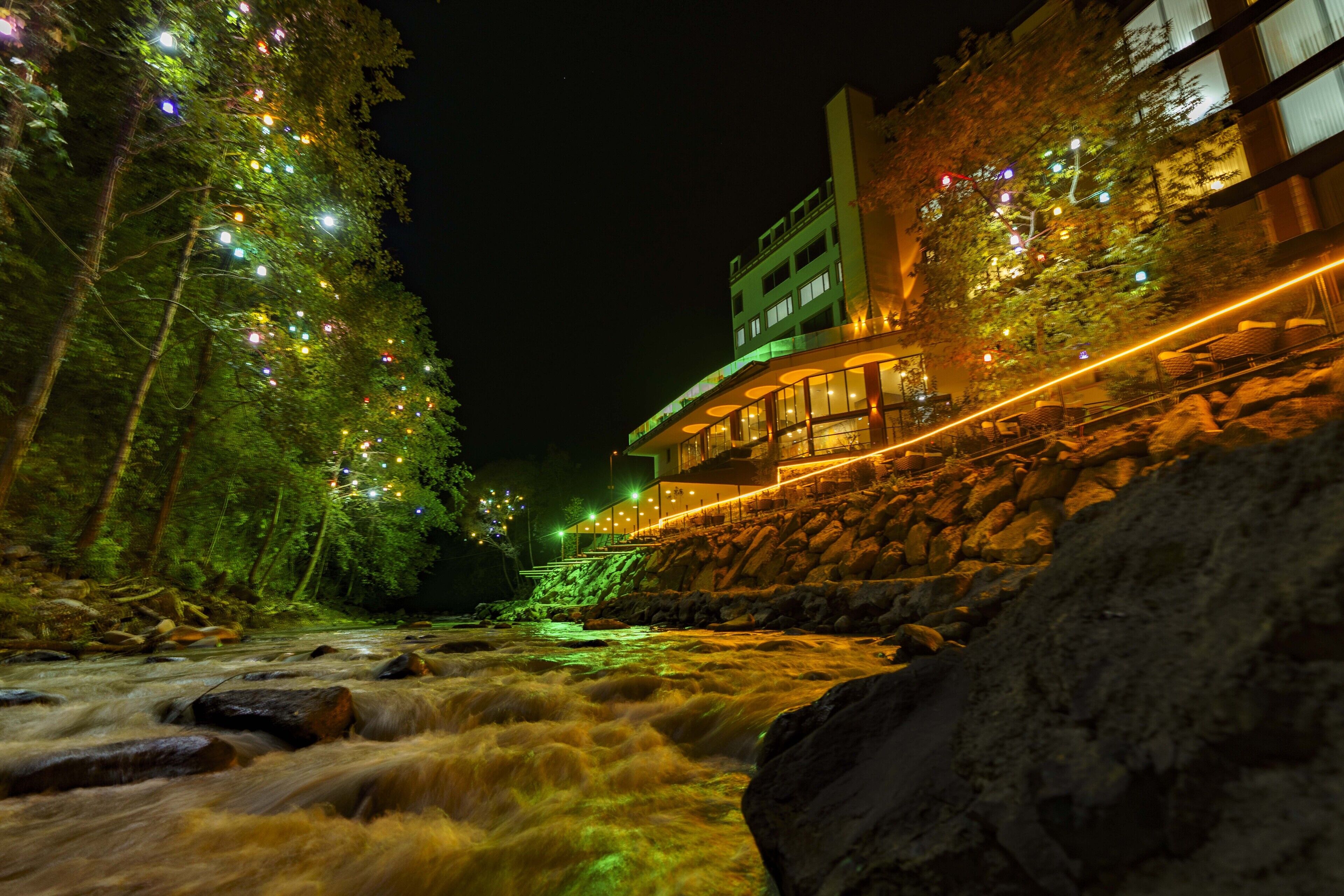Un hotel junto al río con vistas a un río serpenteante, rodeado de árboles y un muro de piedra.