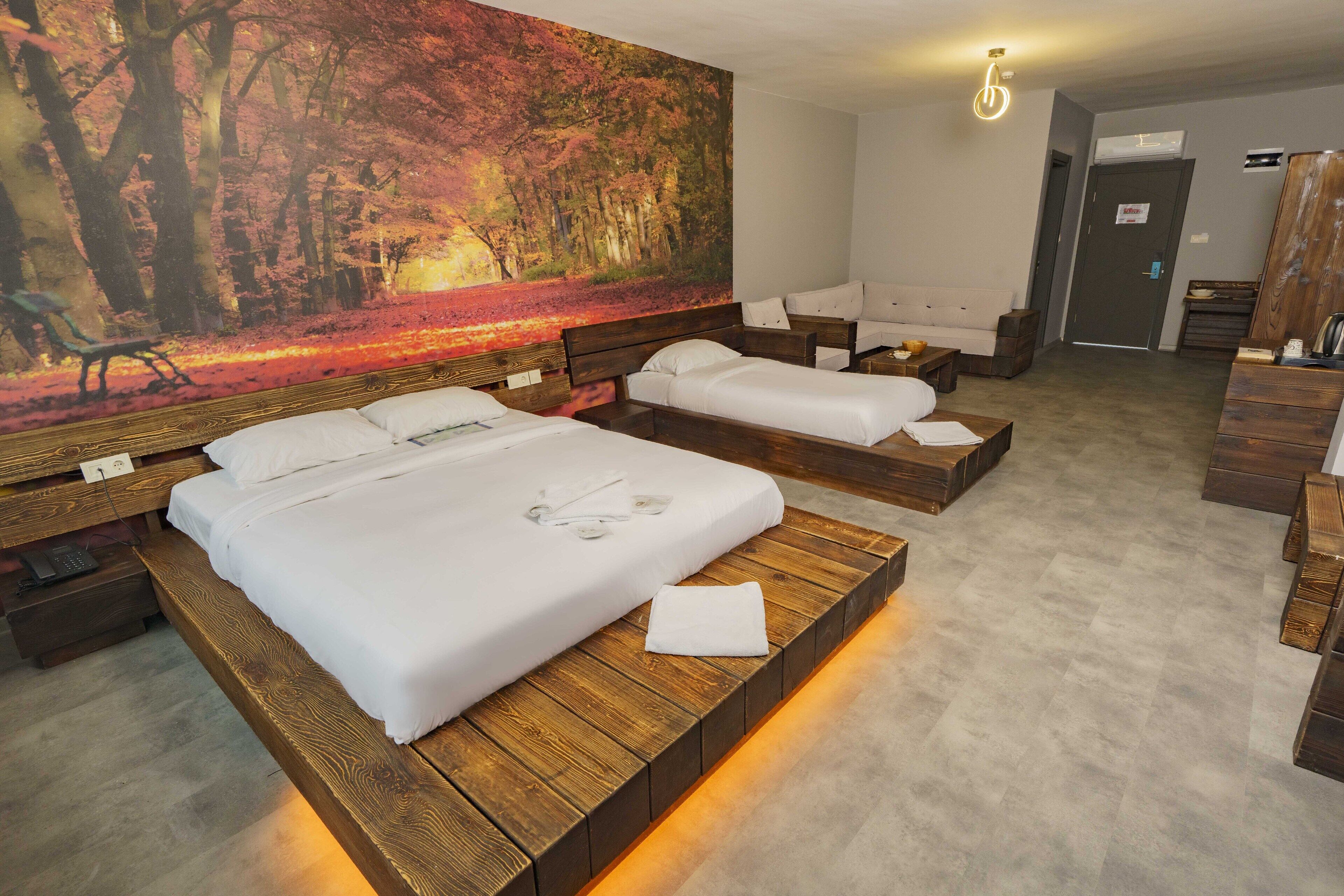 Ein Hotelzimmer mit zwei Betten, einem großen Wandbild zum Thema Wald, einer Holzbank und einem kleinen Tisch mit Lampe.