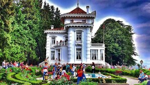 A large, ornate building with a tower, surrounded by lush gardens and a crowd of people. - MacarTaşı Hotel  (Maçka)