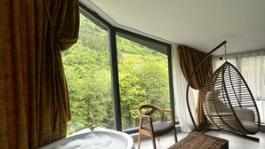A modern room with a large window, a wooden chair, a hanging chair, and a bathtub. - MacarTaşı Hotel  (Maçka)