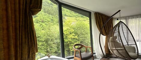 Una habitación moderna con un ventanal grande, una silla de madera, un sillón colgante y una bañera.