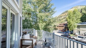 A balcony with outdoor seating, a table with a bottle and glass, and a view of a parking area and buildings in the background. - Lux Home W/ Gas Fireplace, Hot Tub, 8 Min To Lift 7 Bunk Room For Kids! 4 Bedroom Home by RedAwning (Telluride)