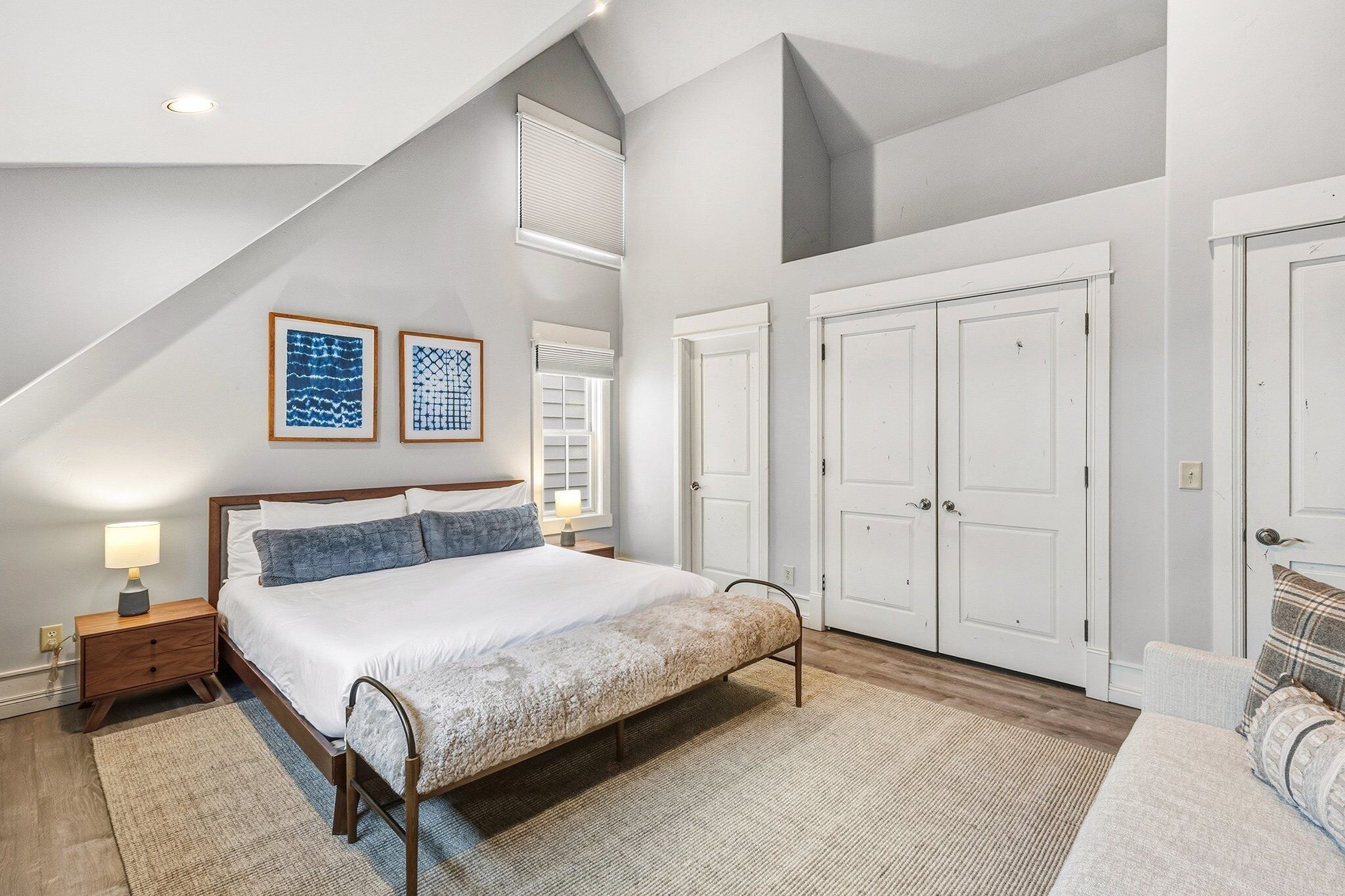 A bedroom with a large bed, a nightstand, a bench, and a dresser.