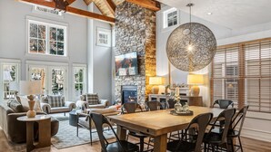 A spacious living room with a fireplace, a dining area, and large windows offering a view of the outdoors. - Lux Home W/ Gas Fireplace, Hot Tub, 8 Min To Lift 7 Bunk Room For Kids! 4 Bedroom Home by RedAwning (Telluride)