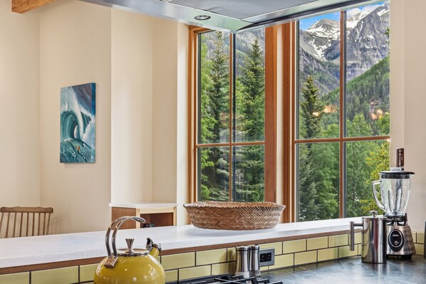 A kitchen with a large window, a kettle, a blender, and a woven basket.