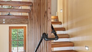 A wooden staircase with a handrail, a door with a window, and a light fixture on the wall.
