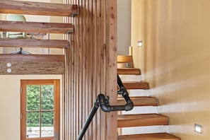 A wooden staircase with a handrail, a door with a window, and a light fixture on the wall.