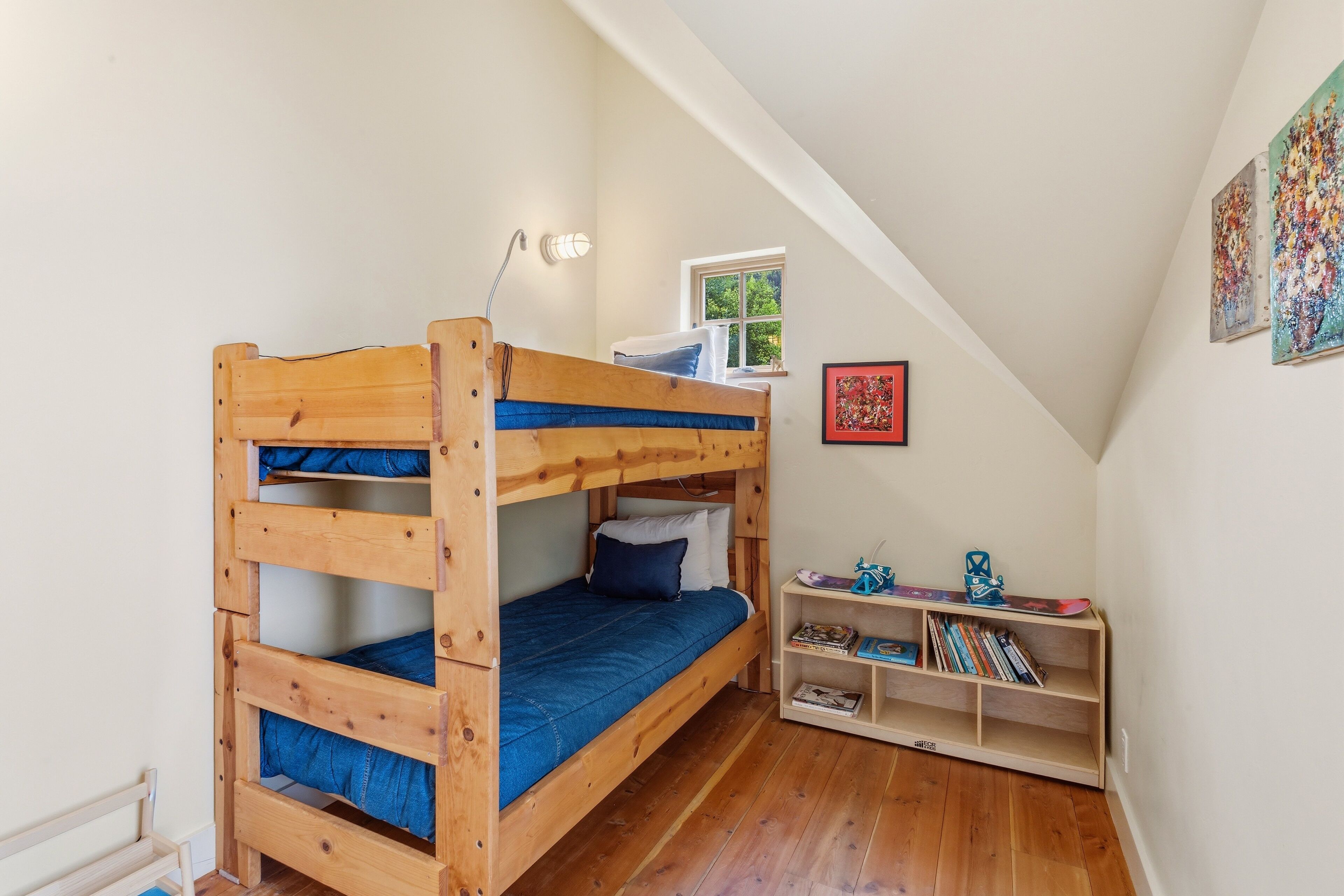 A bunk bed with a desk and shelving unit in a room with wooden flooring and white walls.