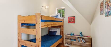 A bunk bed with a desk and shelving unit in a room with wooden flooring and white walls.