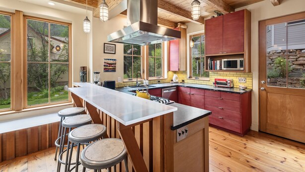 Una cocina moderna con una isla central, taburetes de bar, vigas de madera y ventanas amplias.