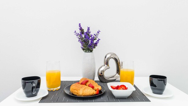 A breakfast table with croissants, strawberries, two glasses of orange juice, and a vase with purple flowers. - Bovolini's Room (Dubrovnik)